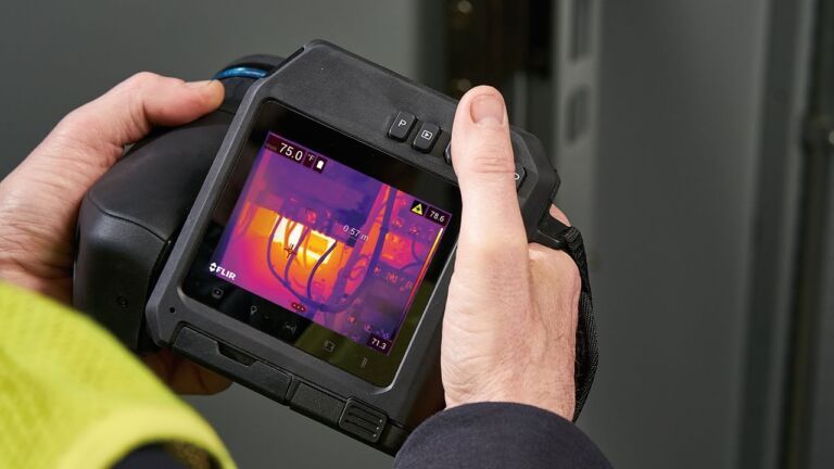 Een persoon houdt een FLIR T-serie camera vast. Op het camerascherm staat een thermisch beeld.